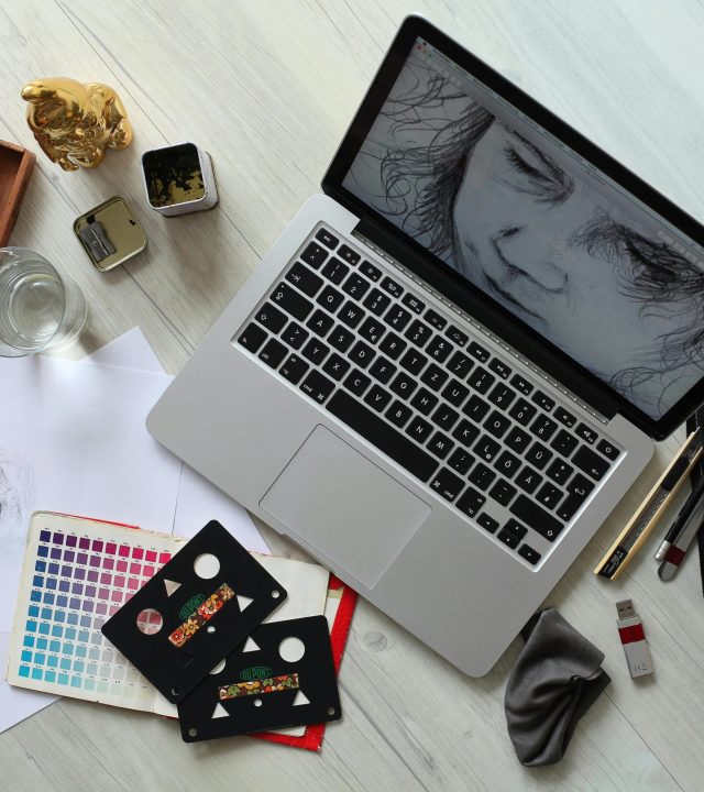 Top view of a creative workspace with a laptop, sketch supplies, and color palette.